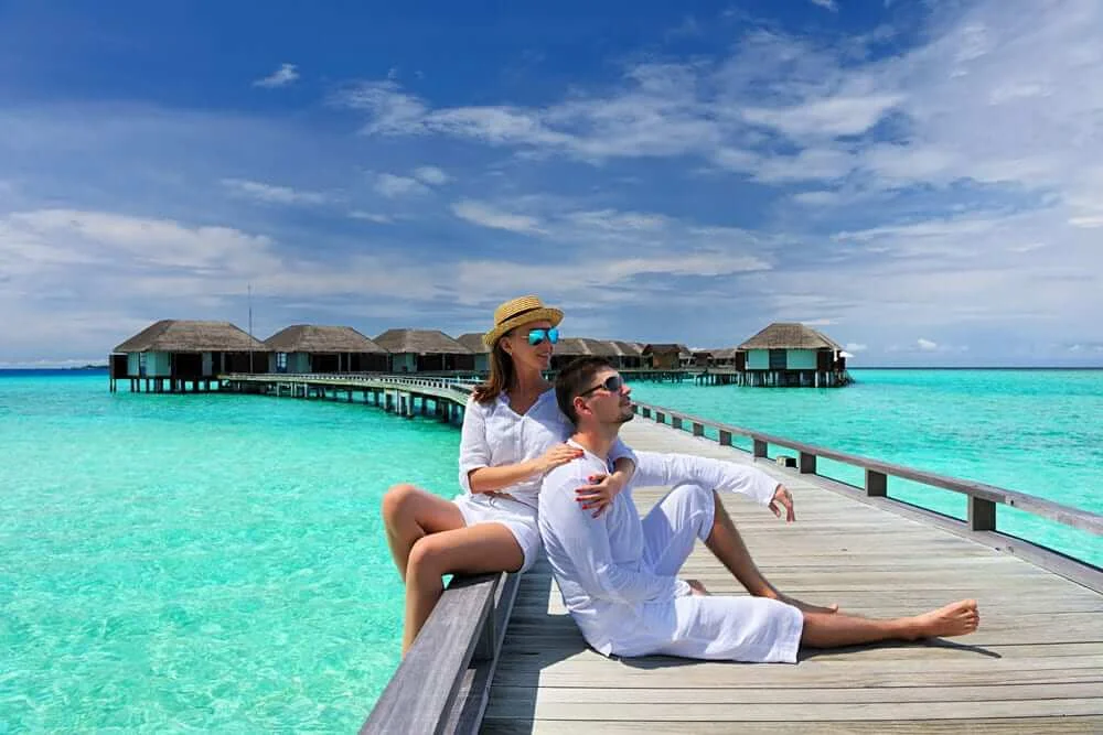 Couple relaxing on a wooden jetty over clear turquoise water near overwater bungalows