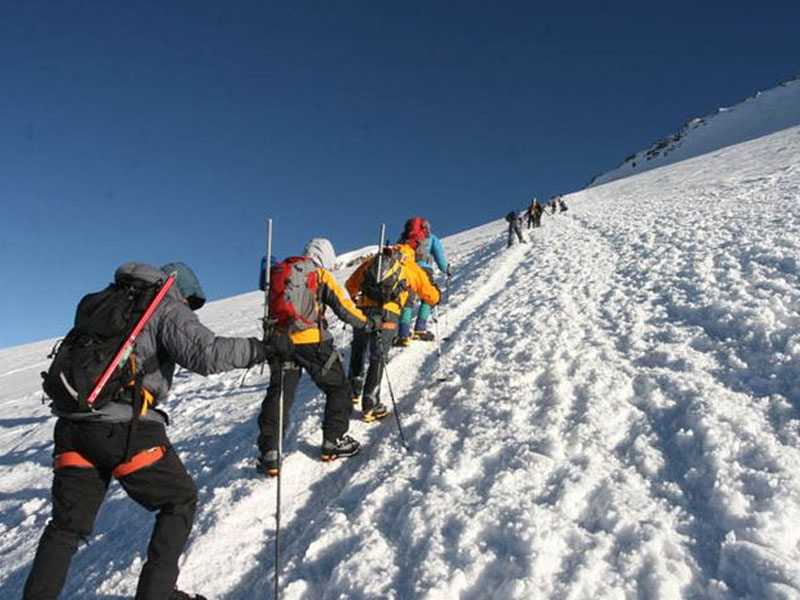 Climbers ascending a snow-covered ridge under a clear sky